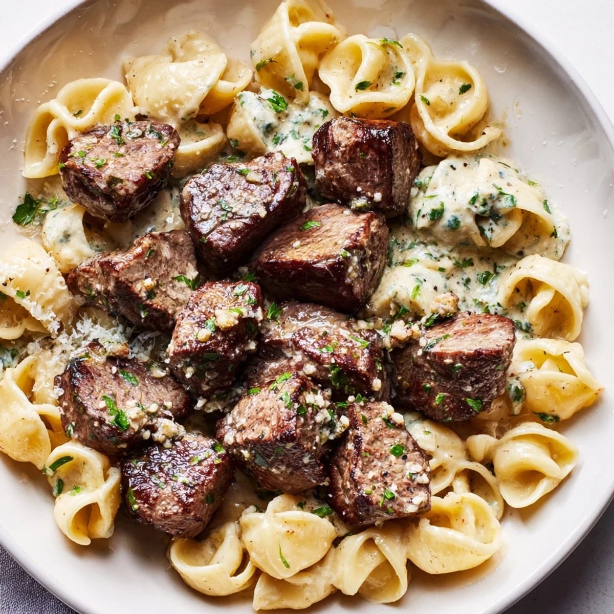 Garlic butter steak bites glistening from the skillet, served alongside creamy, cheesy pasta shells.