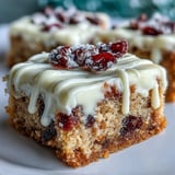 Frosted Cranberry Bliss Bars are drizzled with white chocolate, plated beside a steaming mug of coffee.