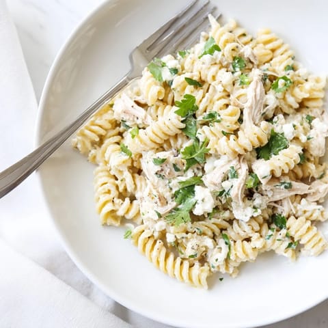 Shredded chicken and rotini pasta tossed in tangy cilantro lime yogurt sauce, served warm in a white bowl.