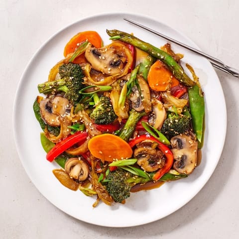 A close-up of Ginger Stir-Fried Vegetables served over jasmine rice, garnished with green onions and toasted sesame seeds.  
