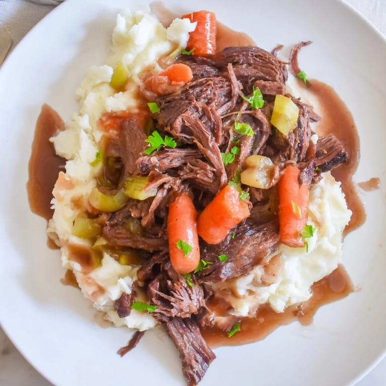 Savory slow cooker pot roast resting alongside rich, fluffy mashed potatoes drizzled with gravy.