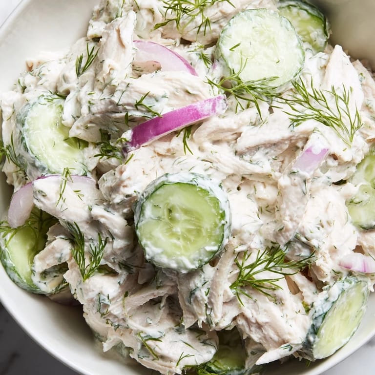 A plated serving of creamy cucumber chicken salad garnished with fresh dill and green onions.  