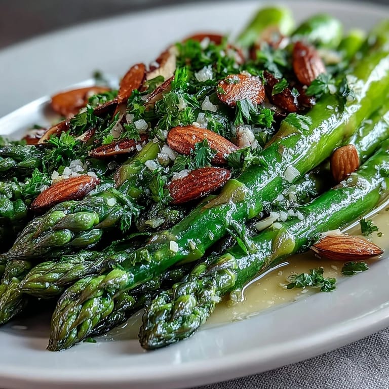 Crisp-tender asparagus spears glisten with lemon butter sauce, garnished with golden toasted almonds for a springtime favorite.